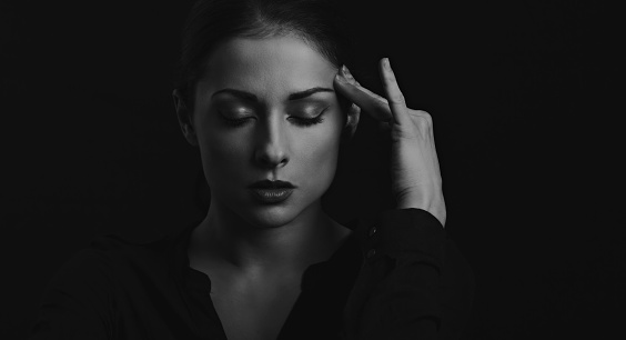 Business strong thinking woman find the answer in clever mind with closed eyes with fingers near the face  in black t-shirt on dark shadow black background. Closeup front view face portrait. Black and white. Art
