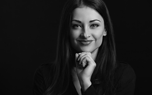 Beautiful confident happy smiling business woman with hand under the face on black background with empty copy space. Closeup portrait. Front center view portrait. Black and white