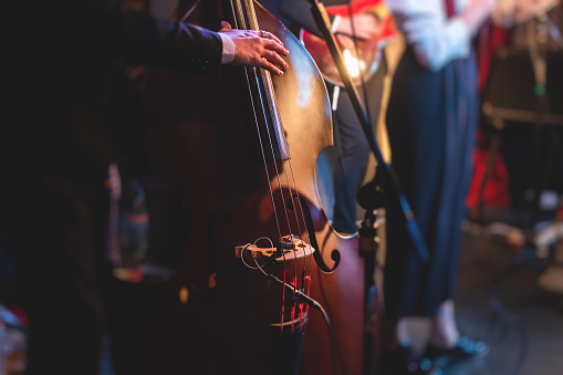 Concert view of a contrabass violoncello player with vocalist and musical band during jazz orchestra band performing music, violoncellist cello jazz player on stage\