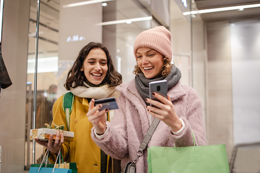 Two young woman using smart phone while doing shopping