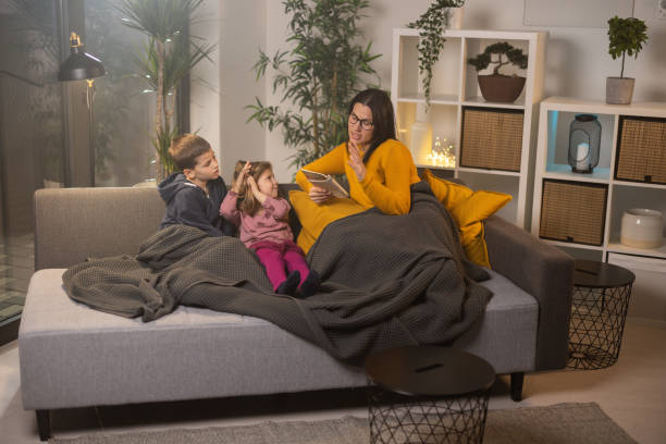 istock Mother sitting on sofa with her kids and reading story from book 1359889157