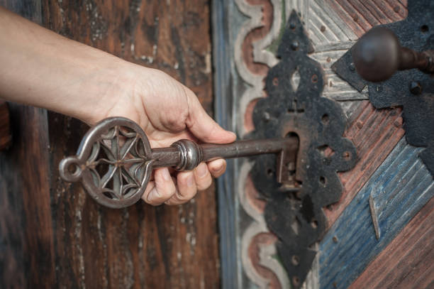 Closeup detail view of man holds a huge massive medieval church key in his hand and unlocks or locks a large wooden door. Secret and mystery