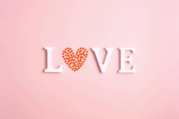 Photo of Word Love made of white letters and heart shaped confetti on pink background. Happy Valentines Day concept. Minimal style.