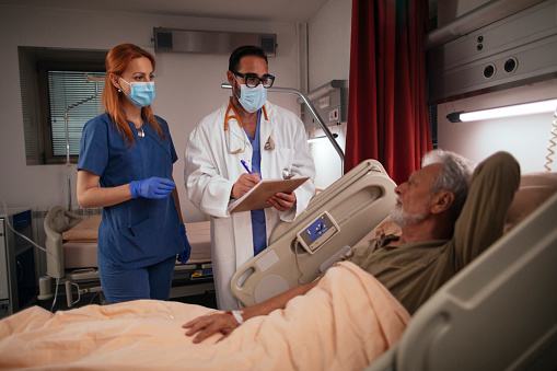 Doctor and nurse visiting their senior patient while he is laying in his hospital bed