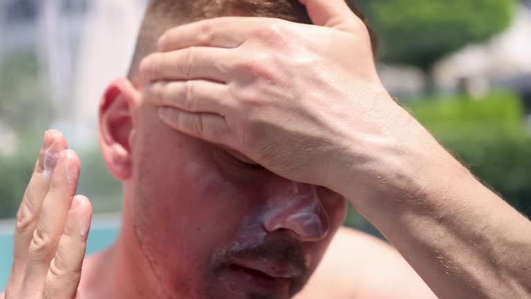 Young man smearing face with sunscreen on beach 4k movie
