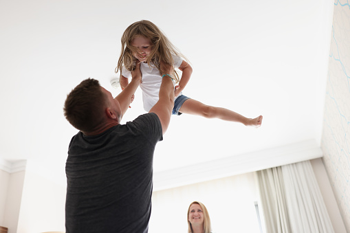 Portrait of father throws child in air and play with kid after work. Happy and healthy relationship in family. Parenthood, childhood, quality time concept