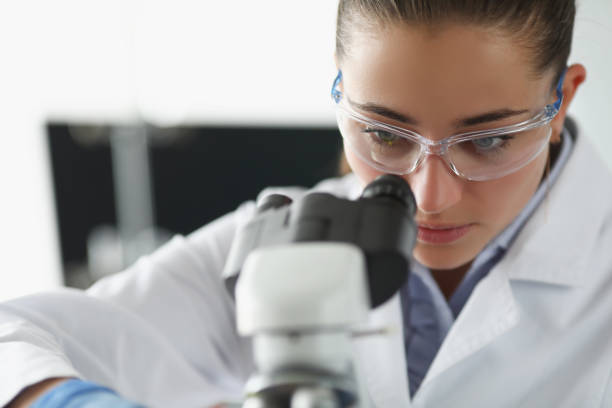 istock Female chemist investigate sample under microscope equipment in lab 1359908600