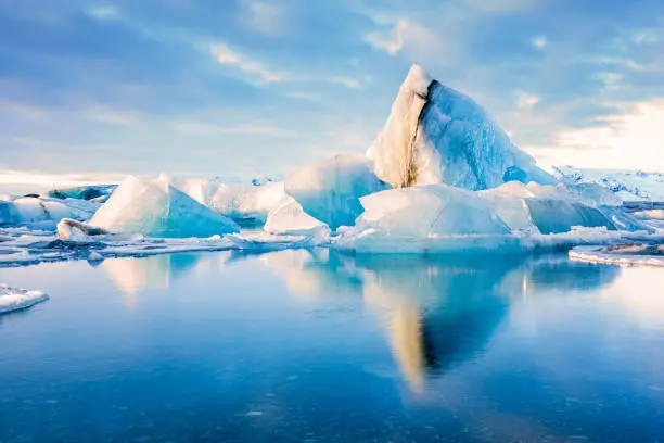 Icebergs float on Jokulsarlon glacier lagoon with mountain peaks lit by the warm sunrise light, in Iceland.
