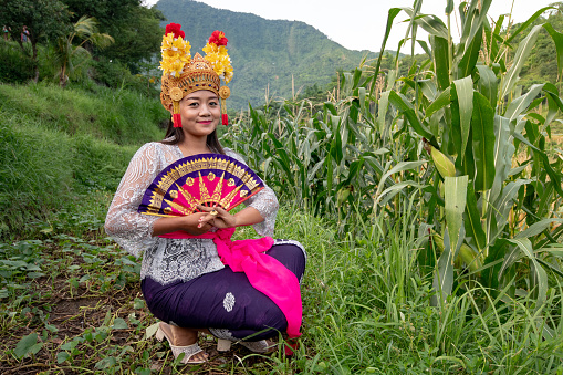 Beautiful balinese dancer woman outdoors with gold headdress and fan
