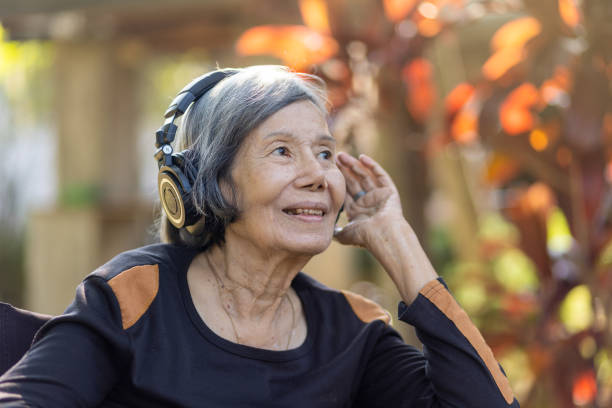 裏庭でヘッドフォンで音楽を聴くアジアの先輩女性。 - alternative medicine audio ストックフォトと画像