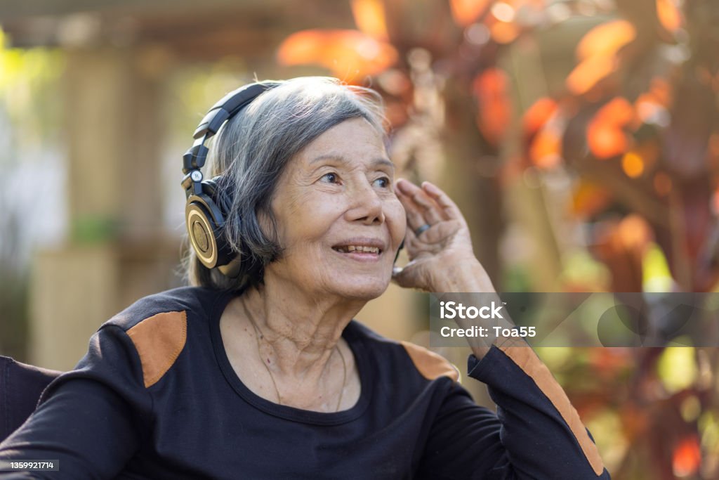 Asian senior woman listening music with headphone in backyard. Dementia Stock Photo
