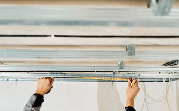 Worker's hands measure and adjust a metal profile for mounting a plasterboard ceiling frame, close-up, selective focus in the hands of a specialist. Industrial renovation and renovation stock photo