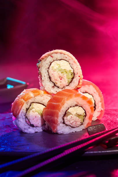 Sushi rolls served at party against multicolored background of neon lighting stock photo