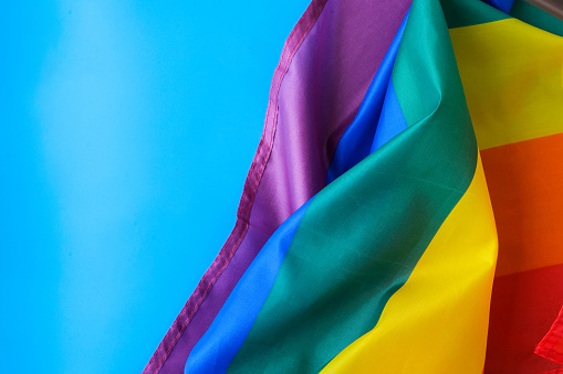 Rainbow flag on blue background with copy space. Rainbow lgbtq flag made from silk material. Symbol of LGBTQ pride month. Equal rights. Peace and freedom