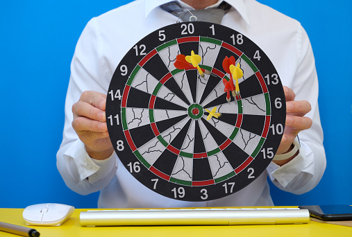 In his workplace, a businessman is holding a dart board and a desk. Workspace with a target and a successful business growth concept, as well as a dart board with a target.