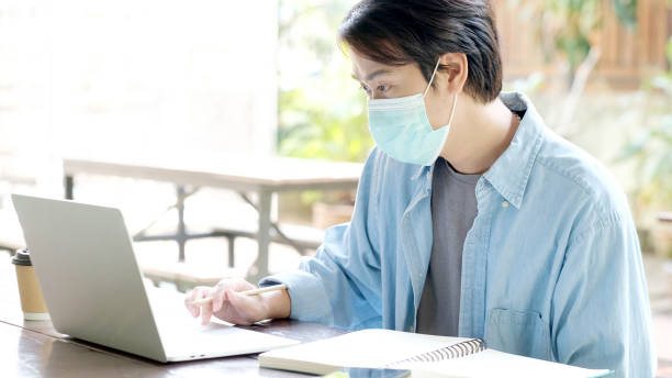 istock Young asian campus student man wearing protection mask working with laptop computer while online study in campus, coronavirus prevention in university, social distancing, online learning 1359947086