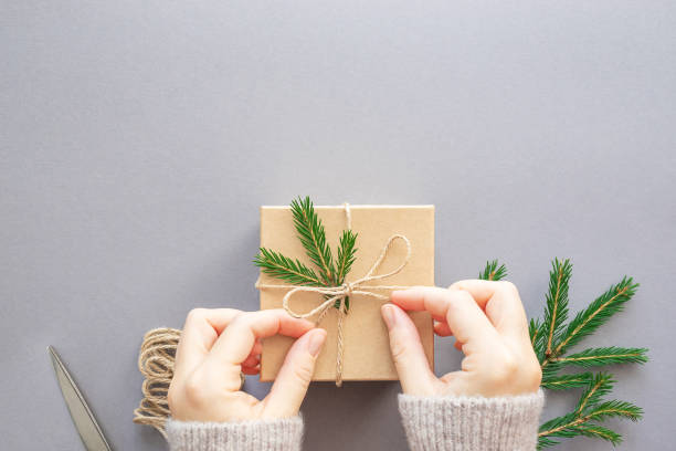 istock Female hands decorate a Christmas gift box, string and spruce branch on a gray background. Zero waste, plastic free. Flat lay, copy space, top view. 1359949070