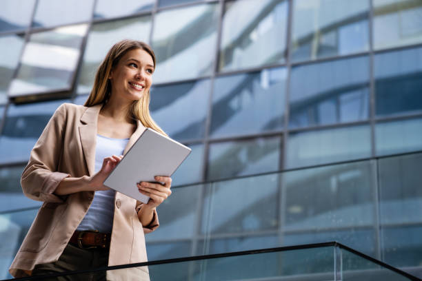 istock Successful businesswoman using a digital tablet while standing in front of business building. 1359951087
