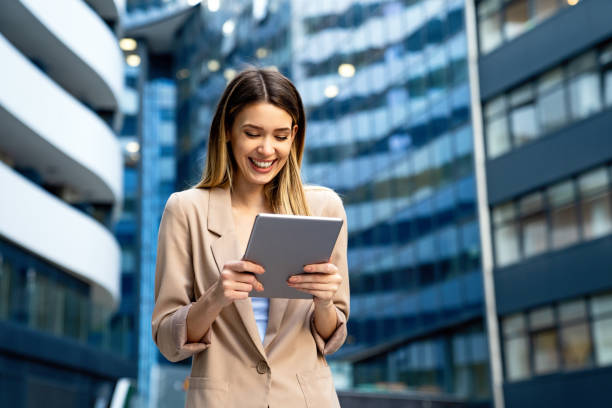 istock Successful businesswoman using a digital tablet while standing in front of business building. 1359951150