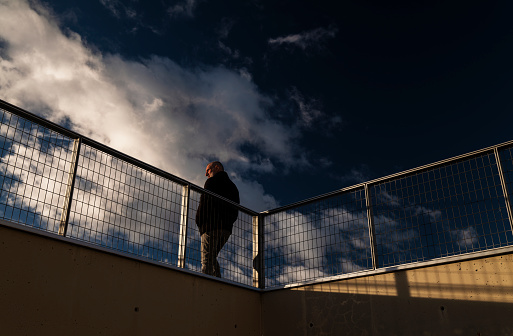 Rear view of adult man standing against fence with blue cloudy sky during sunset. Shot in Madrid, Spain