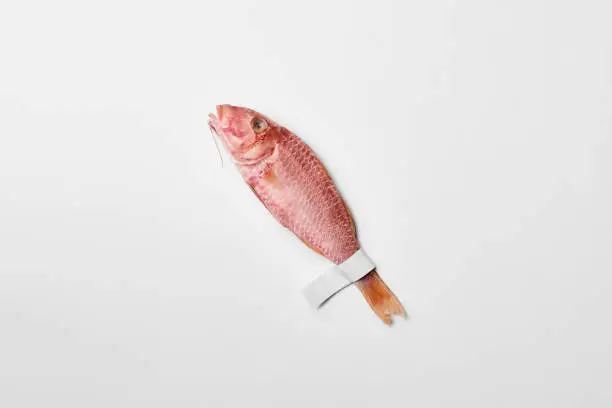 Photo of Salted sun-dried red mullet with paper label on tail on white surface