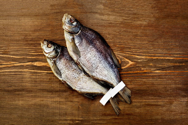 istock Two salted jerked roach fish with labels on tails on wooden background 1359953489