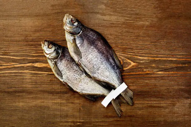 Photo of Two salted jerked roach fish with labels on tails on wooden background