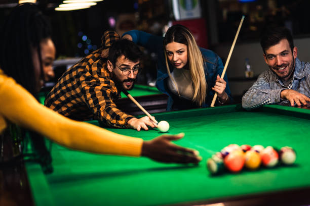 quattro amici sorridenti nel bar che giocano a biliardo insieme. - pool game pool table aiming men foto e immagini stock
