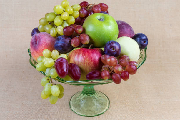 Different fresh fruits in the vintage green glass fruit vase on a cloth surface