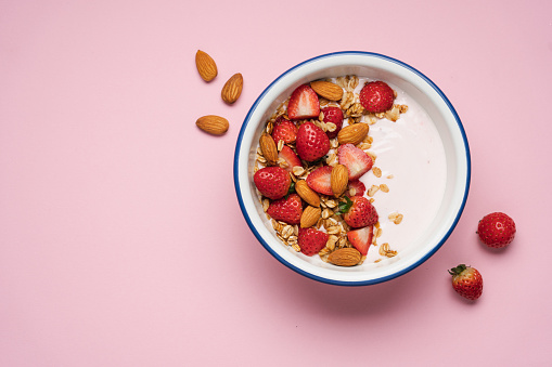Strawberry yogurt with fresh berries, homemade granola, almonds in bowl. Healthy breakfast on pink background