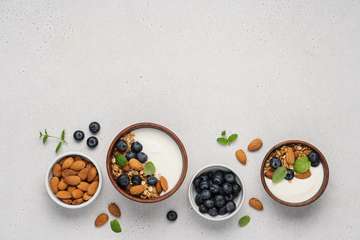 Homemade granola with berries and yoghurt. Bowl of Greek yogurt with almond nuts, oat granola and fresh blueberries on white background