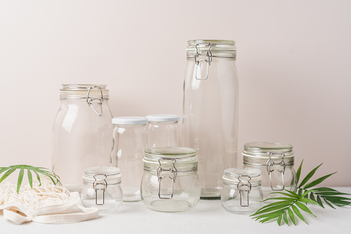 Set of glass jars and bags for zero waste grocery shopping. Side view, light beige background