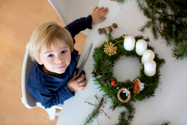 Cute toddler blond child, boy, decorating christmas advent wreath at home in sunny room Cute toddler blond child, boy, decorating christmas advent wreath at home advent candle wreath christmas stock pictures, royalty-free photos & images