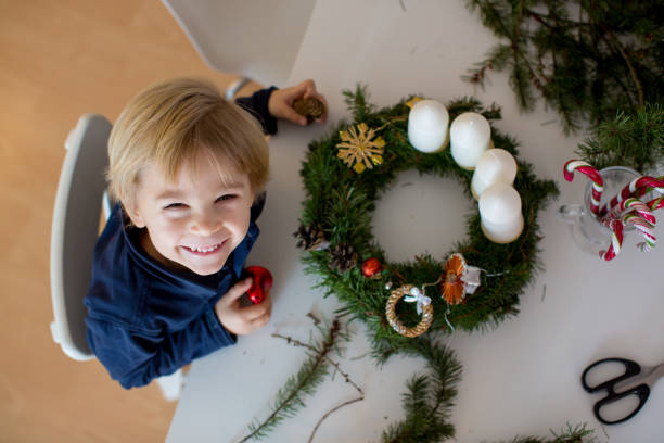 bambino biondo carino bambino, ragazzo, decorare la corona dell'avvento di natale a casa in una stanza soleggiata - advent wreath foto e immagini stock