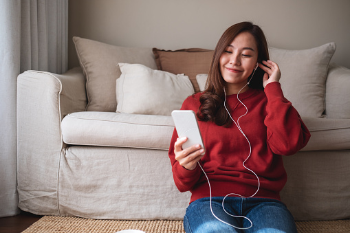 Portrait of a young woman using mobile phone and earphones to listening to music or online chatting at home