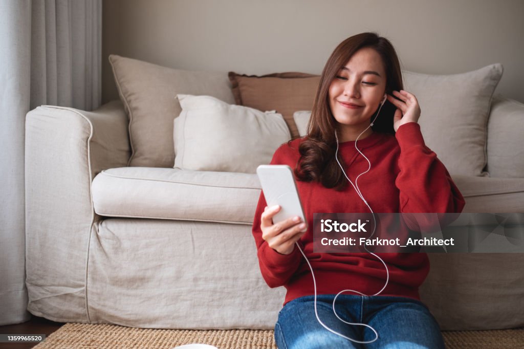 Portrait of a young woman using mobile phone and earphones to listening to music or online chatting at home Music Stock Photo