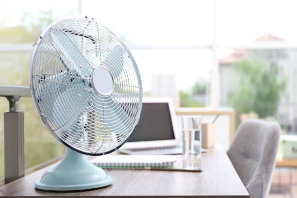 istock Modern fan on wooden table in office, space for text. Summer heat 1359965745