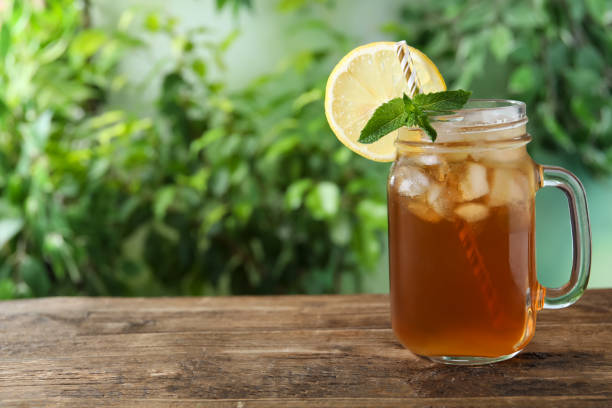 delicioso chá gelado em pote de pedreiro em mesa de madeira ao ar livre, espaço para texto - ice tea ice cube ice tea - fotografias e filmes do acervo