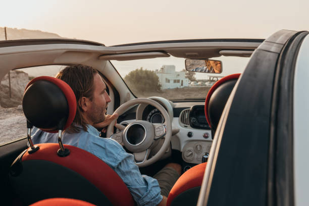istock Young man driving car at sunset, road trip concept 1359969108