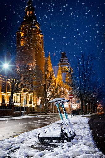 Snow-covered electric scooters on a winter evening in the Haken terrace/ Waly Chrobrego/, monumental Szczecin Voivodeship Office in background, Szczecin, Poland