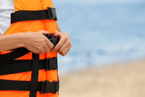 Female lifeguard putting on life vest near sea, closeup