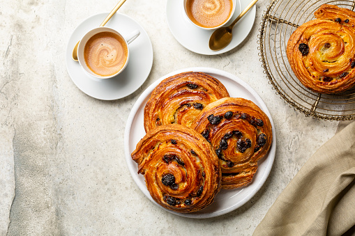 Top view of table with french or continental breakfast with espresso coffee and croissant. Pain aux raisins, also called escargot or pain russe, is a spiral pastry with custard cream and raisin.
