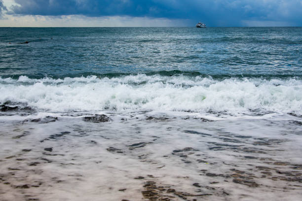 Sea views directly from the beach, sea waves and sandy shore, rain and a ship on the horizon. Coast of the Crimean Peninsula. Travel concept.
