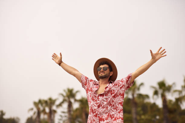 Young man spreading arms wide, smiling under blue sky