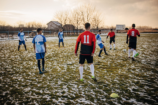 Group of people, male soccer players playing a match on a soccer field on winter day outdoors.