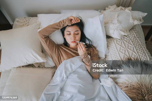 Directly Above Asian Chinese Woman Lying On Bed Covered With Blanket Having Cold And Flu Measured Her Body Temperature With Digital Thermometer Stock Photo - Download Image Now