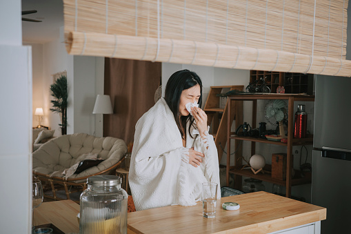 Mujer china asiática cubierta con una manta que tiene resfriado y gripe tomando medicamentos del organizador diario de píldoras en el mostrador de kithen en casa photo
