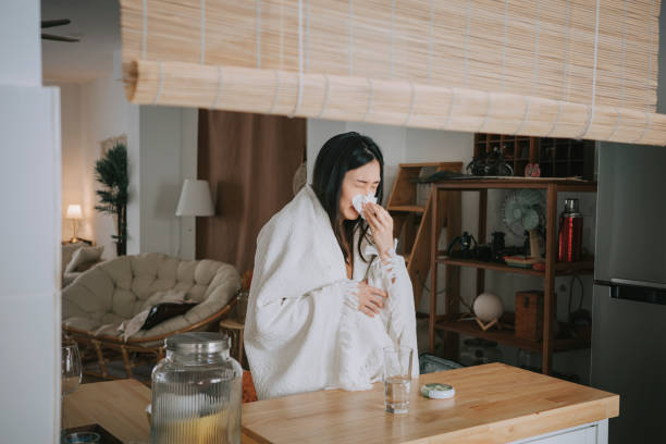 Asian Chinese Woman covered with blanket having  cold and flu taking medicine from daily pill organizer at kithen counter home Asian Chinese Woman covered with blanket having  cold and flu taking medicine from daily pill organizer at kithen counter home allergy medicine stock pictures, royalty-free photos & images