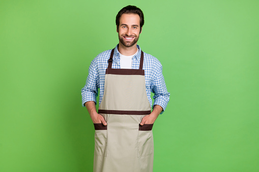 Photo of nice millennial working guy wear shirt apron isolated on green background.