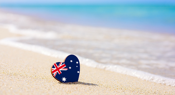 Flag of Australia in the shape of a heart on a sandy beach.